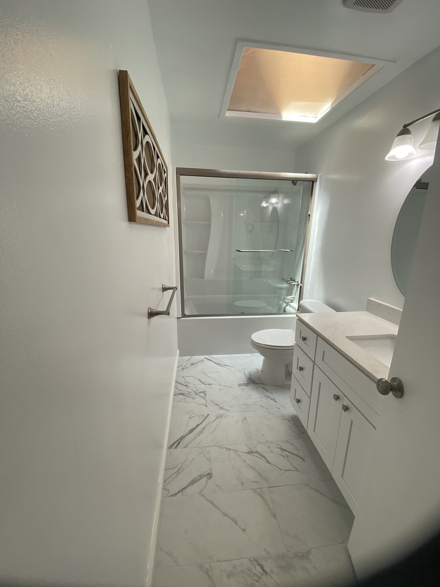 Bathroom Remodel — After: Marble tile, white shaker vanity, glass enclosure